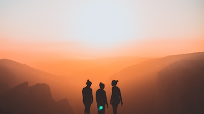 silhouette of three people up on mountain cliff