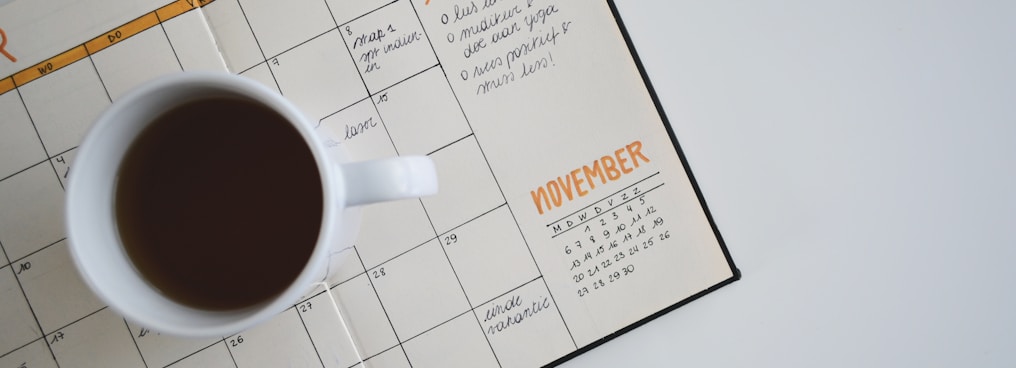 white ceramic mug with coffee on top of a planner