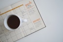 white ceramic mug with coffee on top of a planner