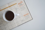 white ceramic mug with coffee on top of a planner