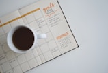 white ceramic mug with coffee on top of a planner