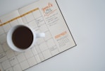 white ceramic mug with coffee on top of a planner