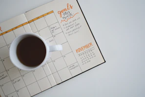 white ceramic mug with coffee on top of a planner