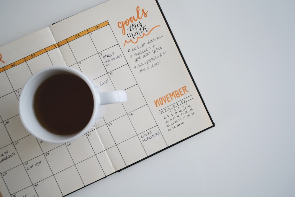 white ceramic mug with coffee on top of a planner