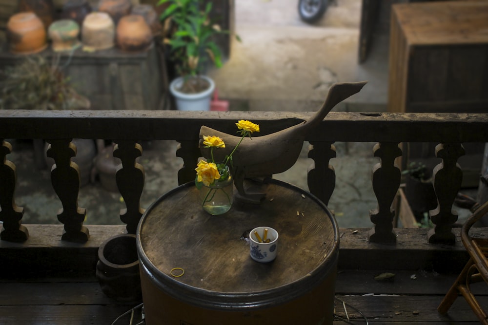 yellow petaled flowers in vase on brown wooden barrel