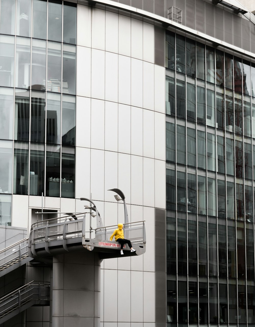 personne assise sur le bord d’un pont près d’un bâtiment pendant la journée