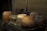 A collection of rustic clay pots, varying in size and shape, is arranged on a wooden surface. The pots exhibit an earthy color palette with shades of brown, green, and ochre, accompanied by signs of wear and age. A thatched or bamboo mat serves as a backdrop, adding to the rustic aesthetic.