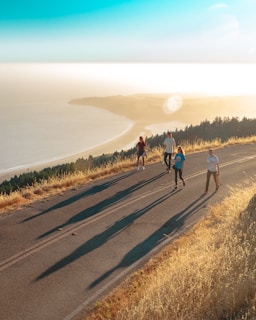 four men and women walking on roadway near body of water