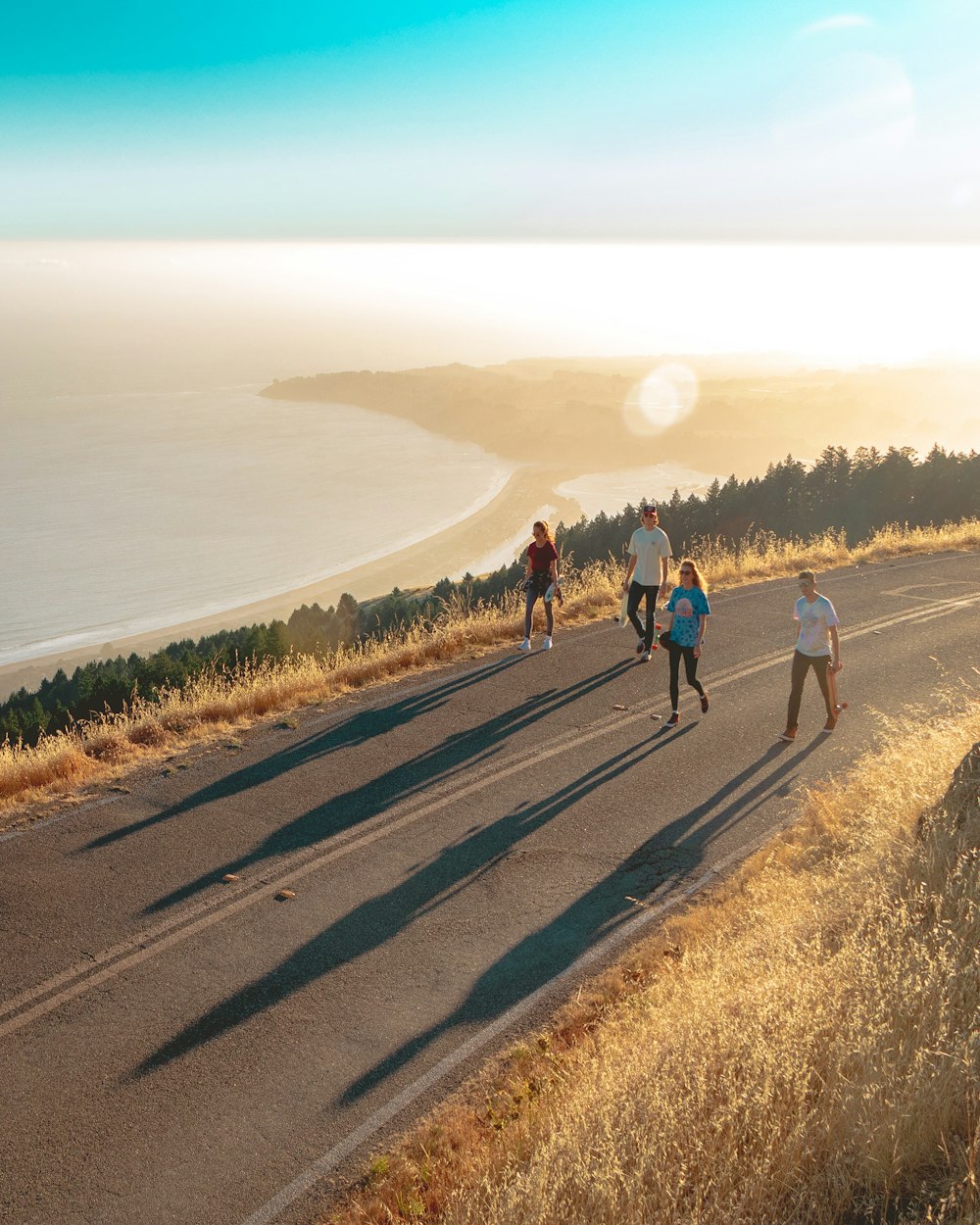 four men and women walking on roadway near body of water