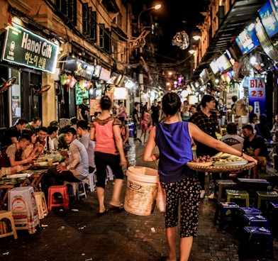 woman carrying woven tray and white pail while walking on wet market