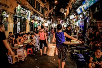 woman carrying woven tray and white pail while walking on wet market