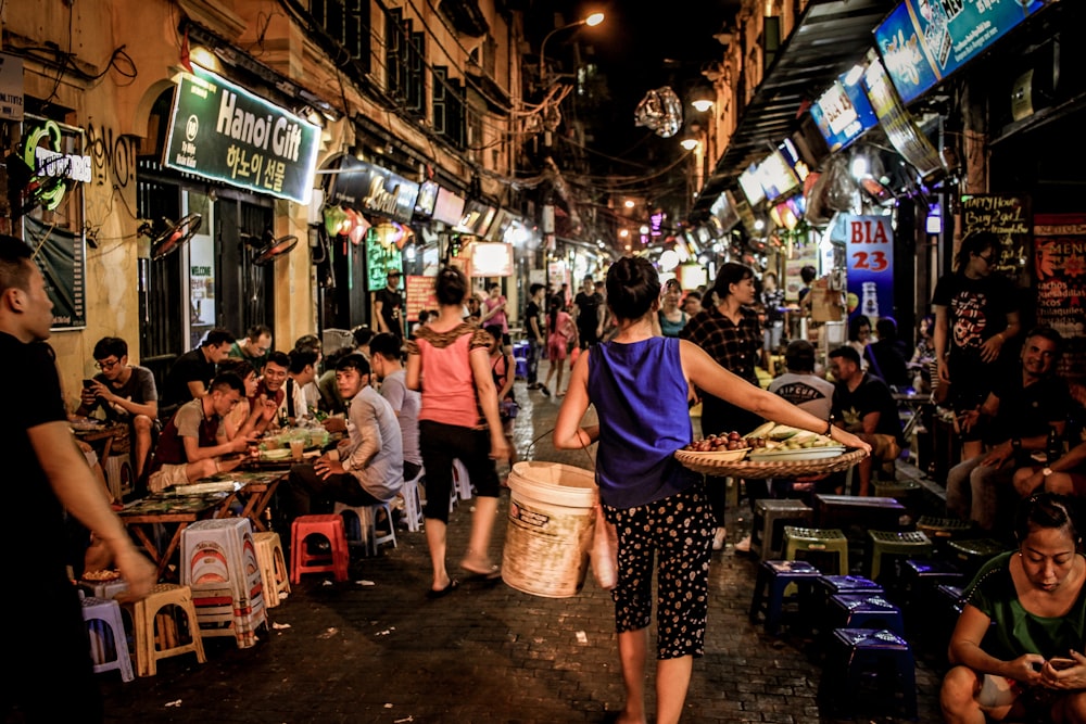 woman carrying woven tray and white pail while walking on wet market