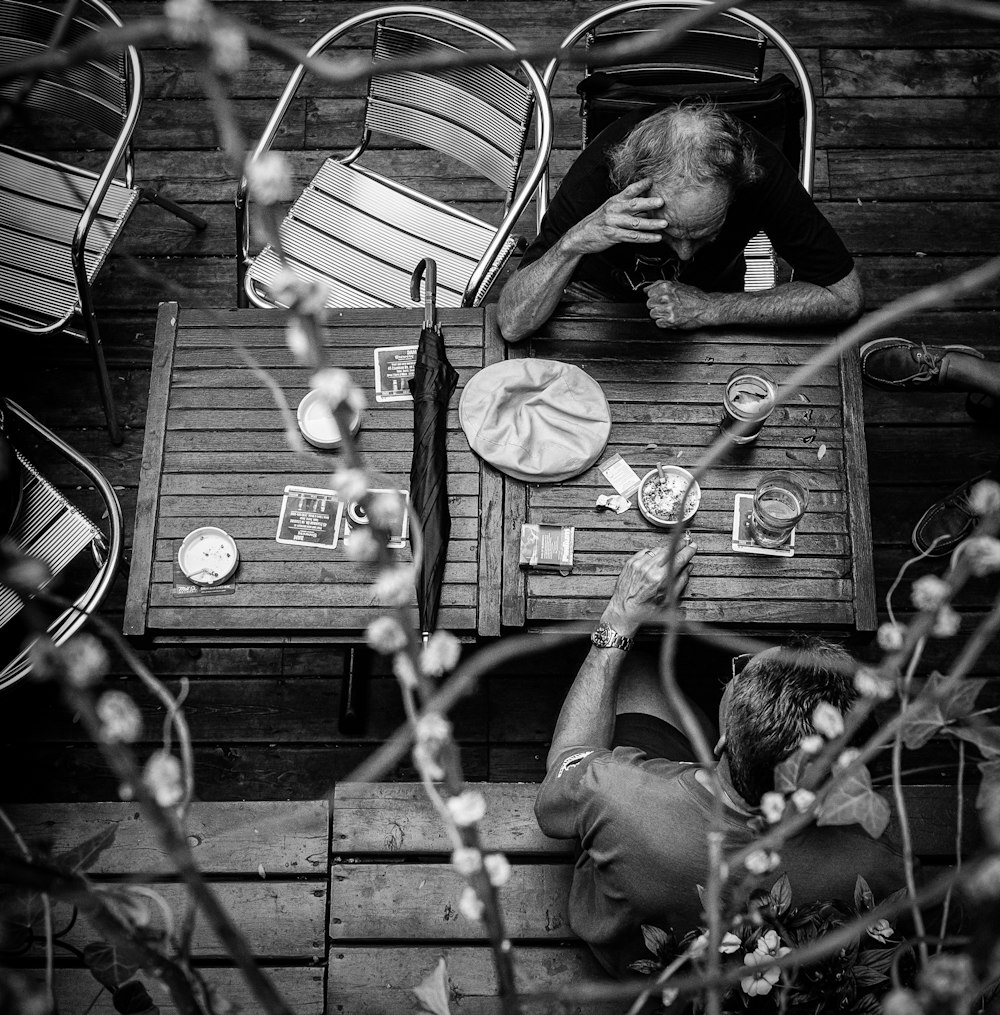 grayscale photo of two men sitting on chair leaning on table