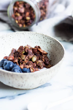 Close-up of a bowl filled with fresh organic granola topped with nuts and dried fruits on a rustic wooden table.