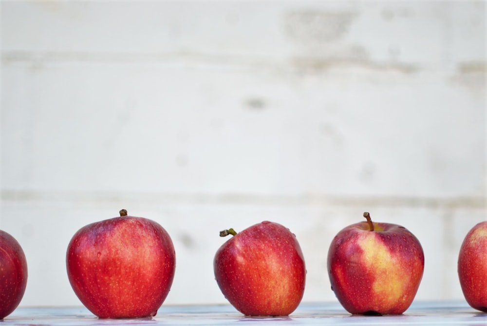 cinq pommes rouges sur une surface blanche