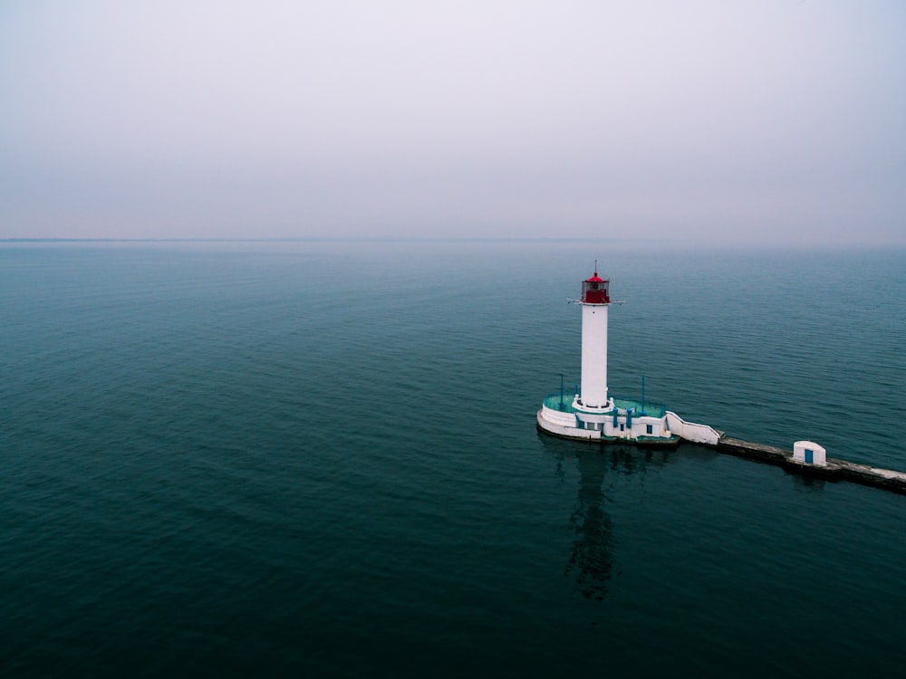 white and green lighthouse with body of water under white sky during daytime