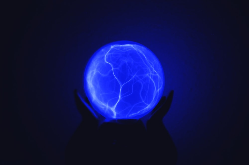 Foto con poca luz de la persona que sostiene la bola iluminada azul