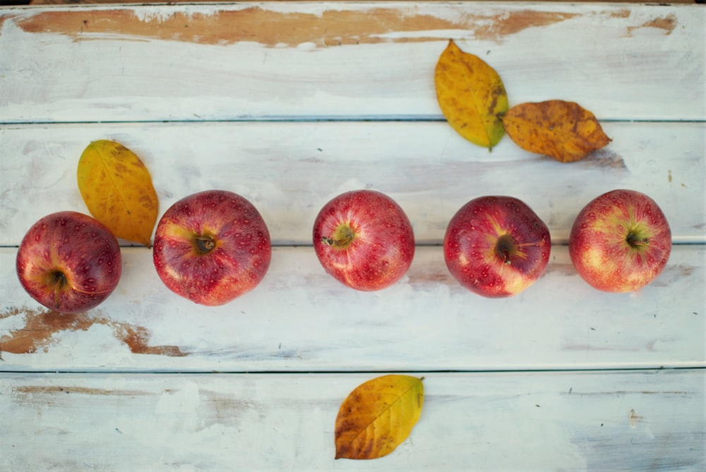 A row of apples on a table, with a few autumn leaves