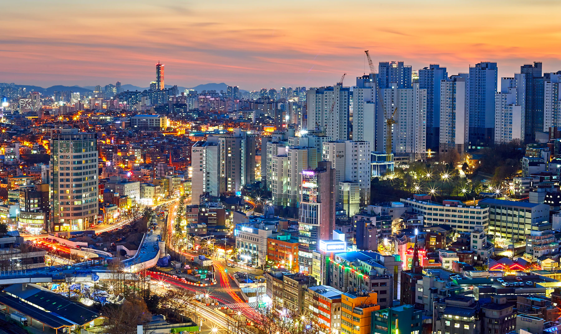Dense Seoul cityscape under a warm orange sky at sunset