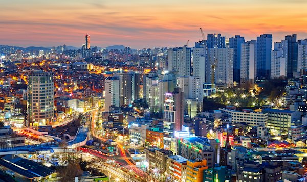 A dense cityscape in Seoul, South Korea, under a warm orange sky at night