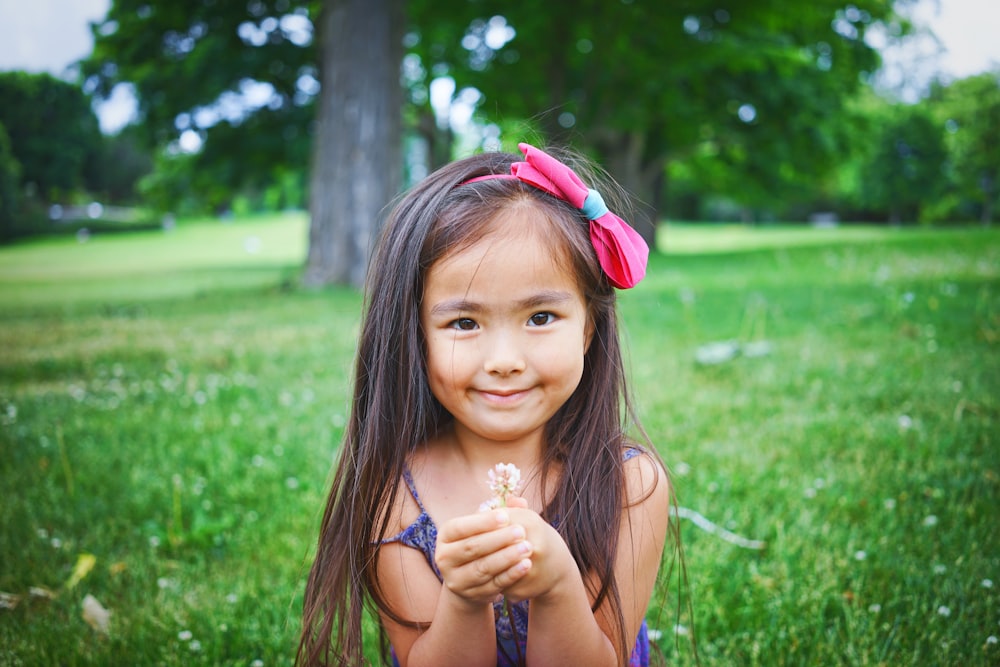 girl wearing black top while standing and holding flower on green grass