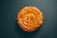 A round pastry with an intricate floral pattern embossed on its surface, set against a dark textured background. The pastry is a golden brown with a glossy finish, featuring the characters '7B' in the center.