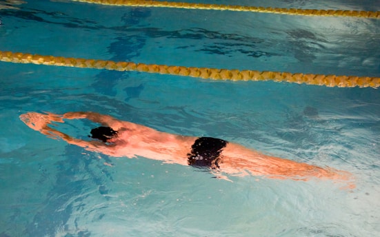 A coach guiding a swimmer in a clear pool, demonstrating proper stroke technique.