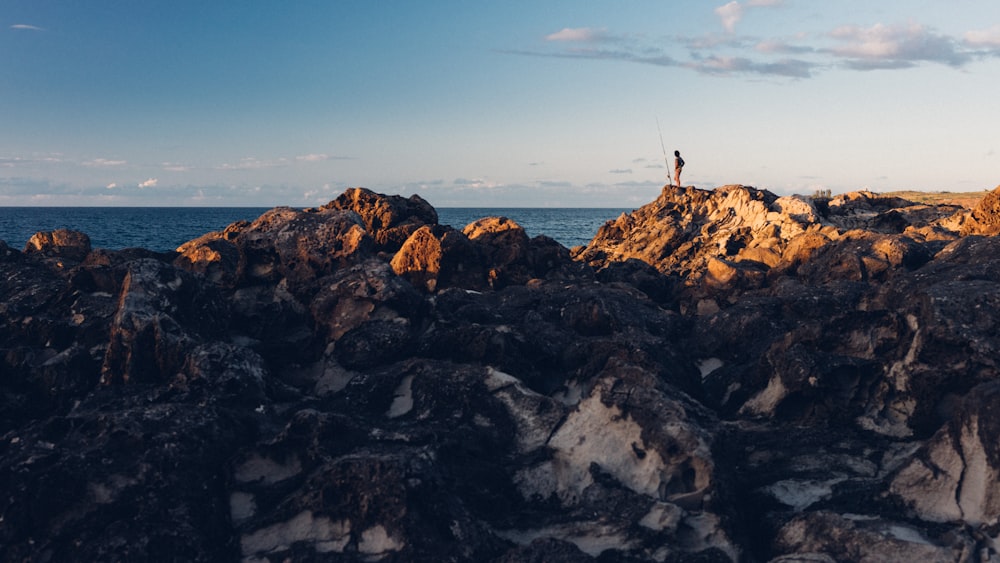 a person standing on top of a rocky beach next to the ocean