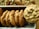 A batch of freshly baked chocolate chip cookies is neatly arranged in a metal tray. The cookies are golden brown with a slightly crispy texture around the edges and chunks of melted chocolate visible on the surface.