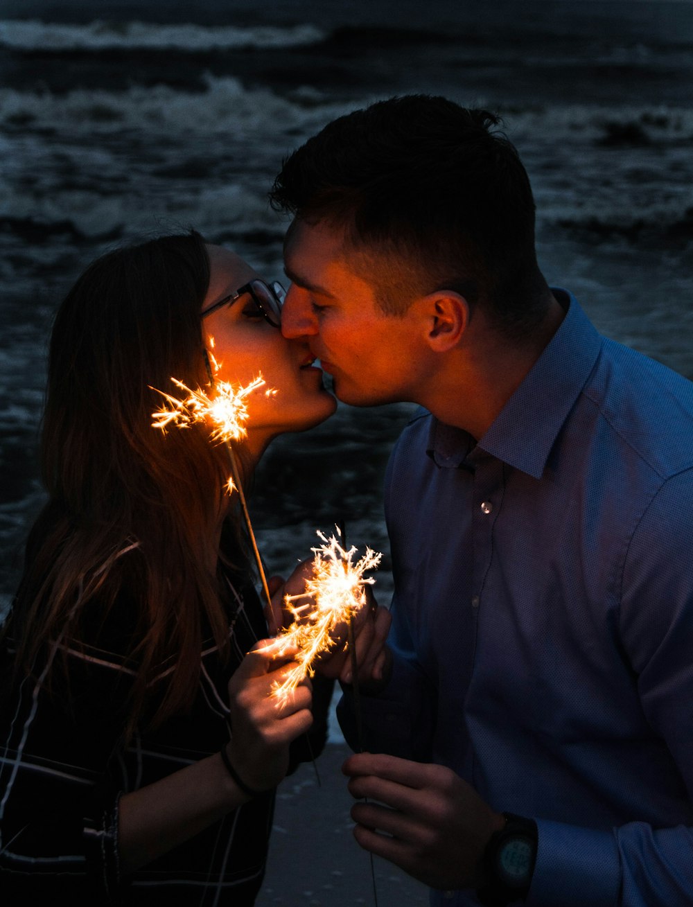 pareja besándose mientras sostiene bengalas durante la noche