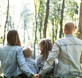 man and woman holding hands together with boy and girl looking at green trees during day