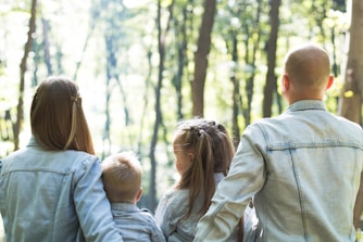 Family - man and woman holding hands together with boy and girl looking at green trees during day