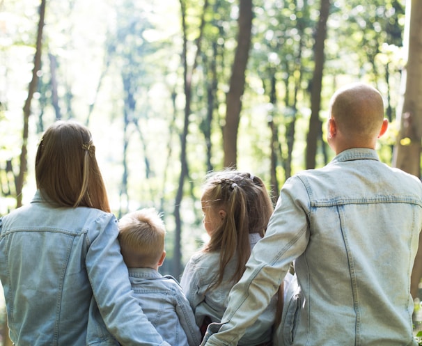 man and woman holding hands together with boy and girl looking at green trees during day