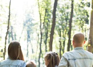 man and woman holding hands together with boy and girl looking at green trees during day