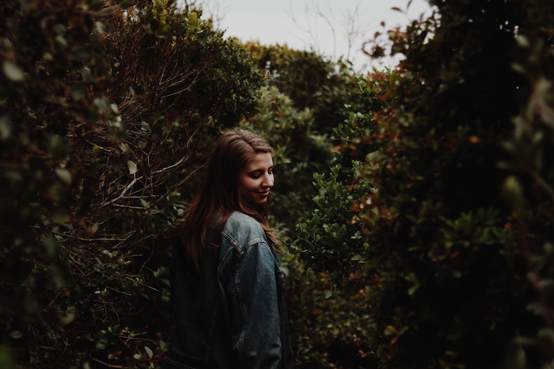 woman walking in between green trees at daytime