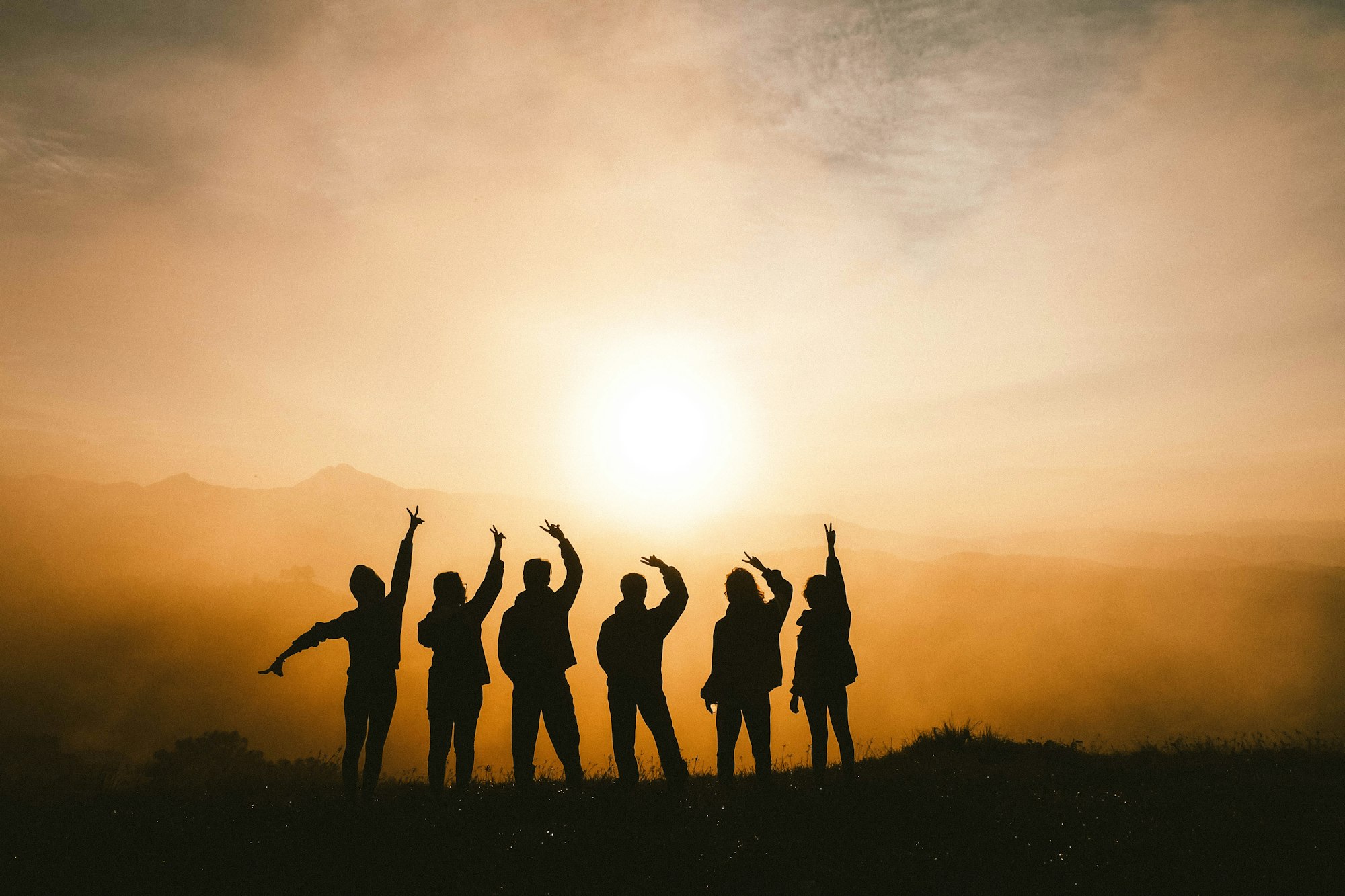 Silhouette of six best friends cheerfully posing with a peace hand sign towards the setting sun.