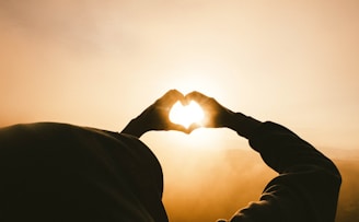 person doing heart shape hand with sun light passing thru