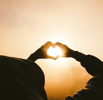 person doing heart shape hand with sun light passing thru