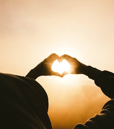 person doing heart shape hand with sun light passing thru