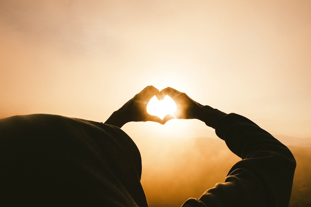 person doing heart shape hand with sun light passing thru