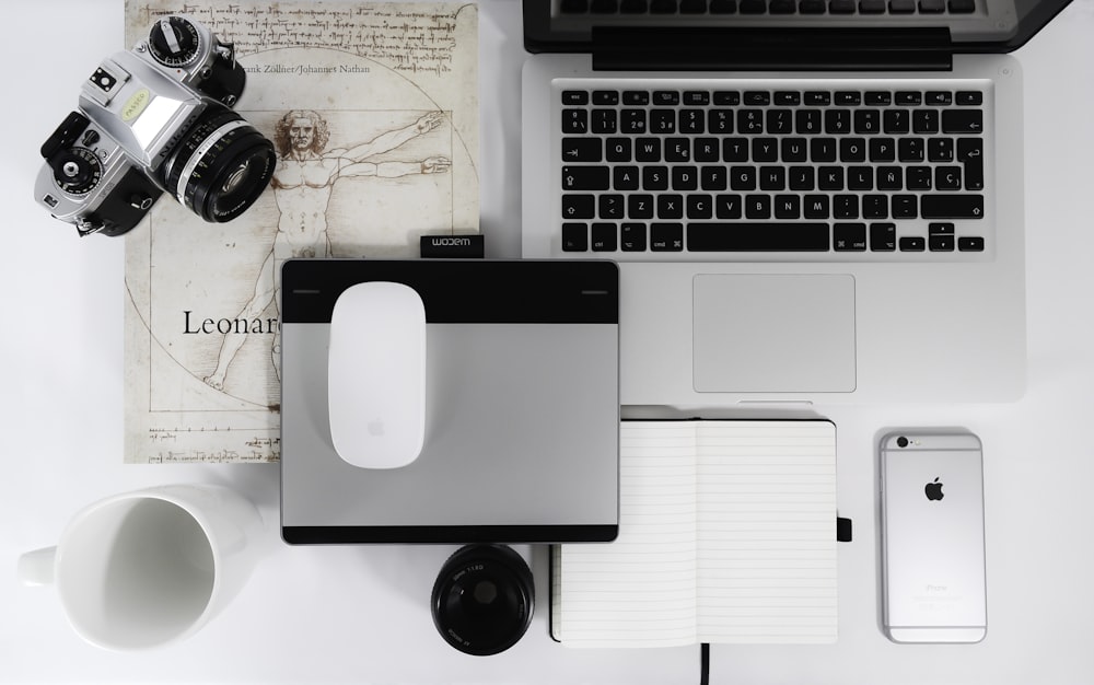 Apple Magic Mouse blanc, trackpad gris, appareil photo reflex gris, iPhone 6s gris sidéral et MacBook Pro sur la table