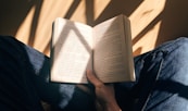 person holding book sitting on brown surface