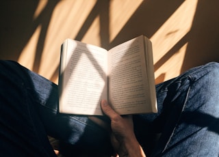 person holding book sitting on brown surface