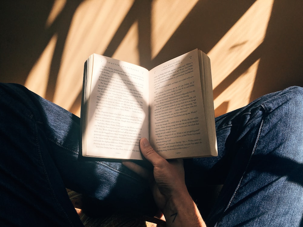 persona sosteniendo un libro sentado en una superficie marrón