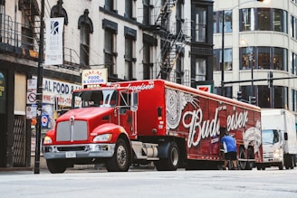 man near red Budweiser trailer truck parked near concrete building during daytime