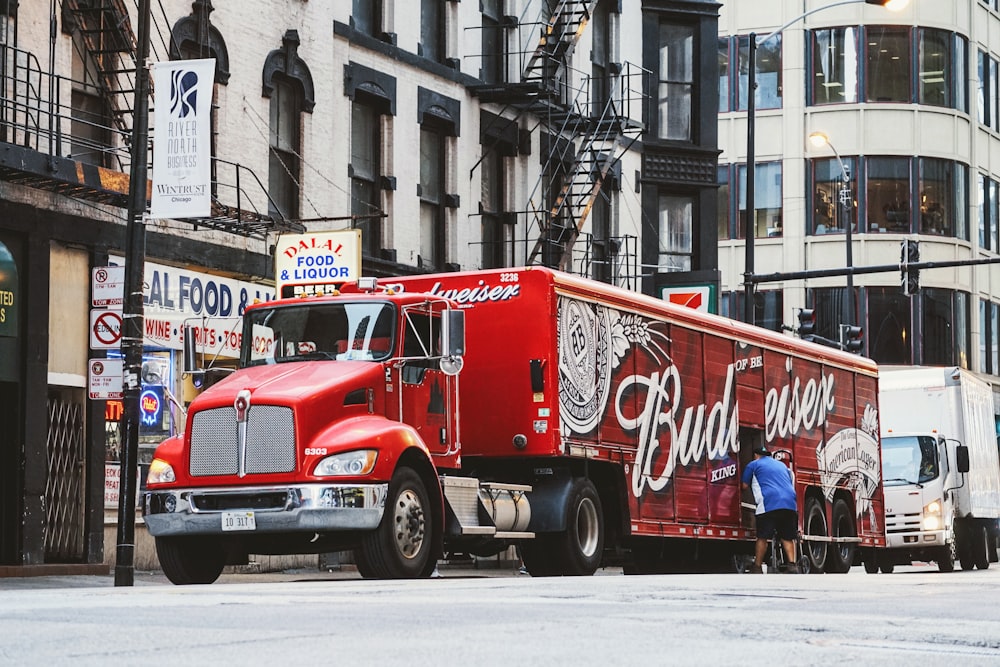 homem perto de caminhão de reboque Budweiser vermelho estacionado perto de prédio de concreto durante o dia