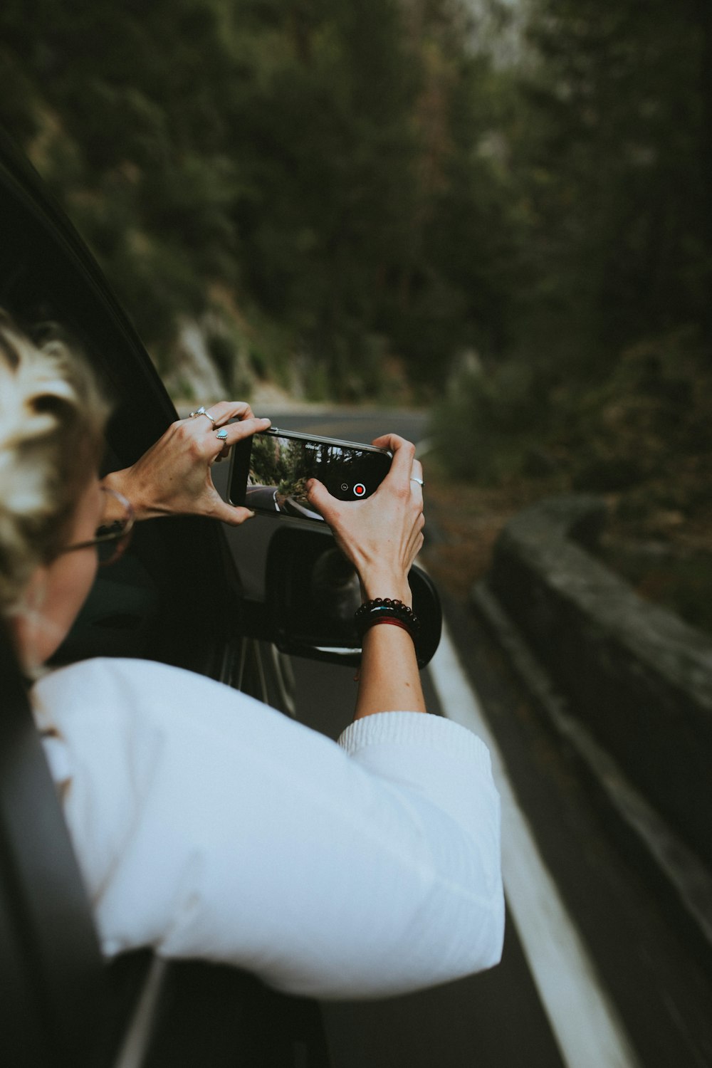 Donna che guida sull'auto che tiene lo smartphone che scatta una foto