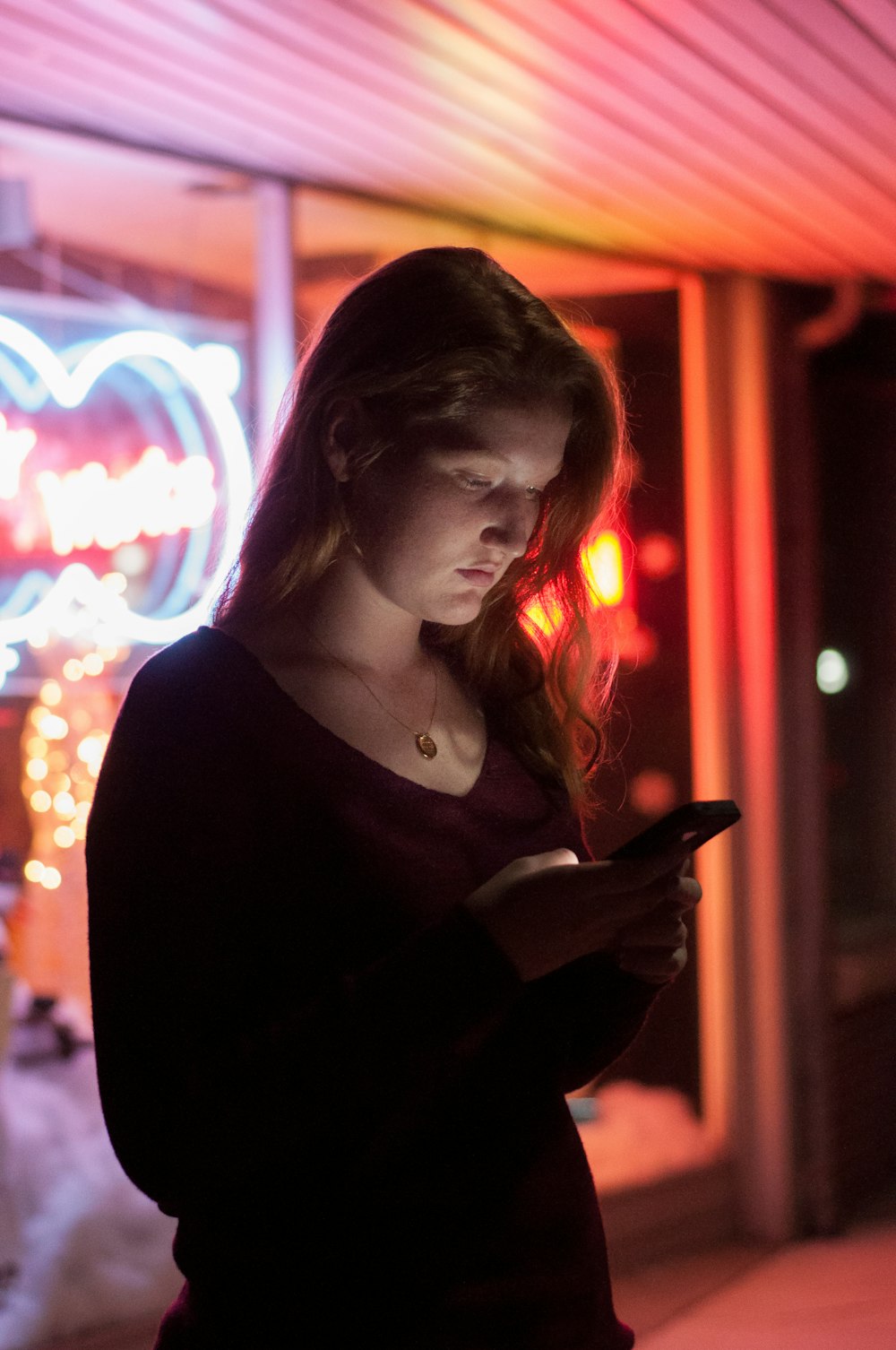 Mujer usando teléfono inteligente frente a una tienda de vidrio con luces rojas y azules