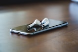 Close-up of a sleek smartphone and wireless earbuds on a wooden table.