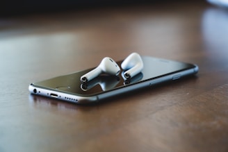 A close-up of a sleek smartphone and wireless earbuds on a wooden table.